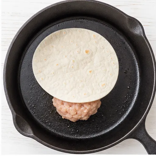 Step 2: Placing a tortilla on a chicken ball in the skillet