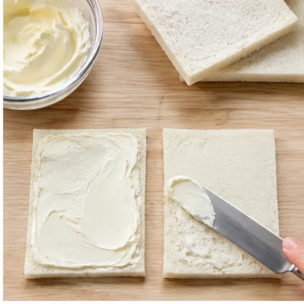 Step 2: Spreading softened cream cheese over thin white bread slices