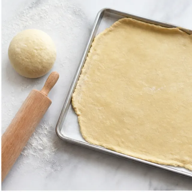 Pressing two store-bought pie crusts into one ball and rolling the dough onto a quarter sheet pan