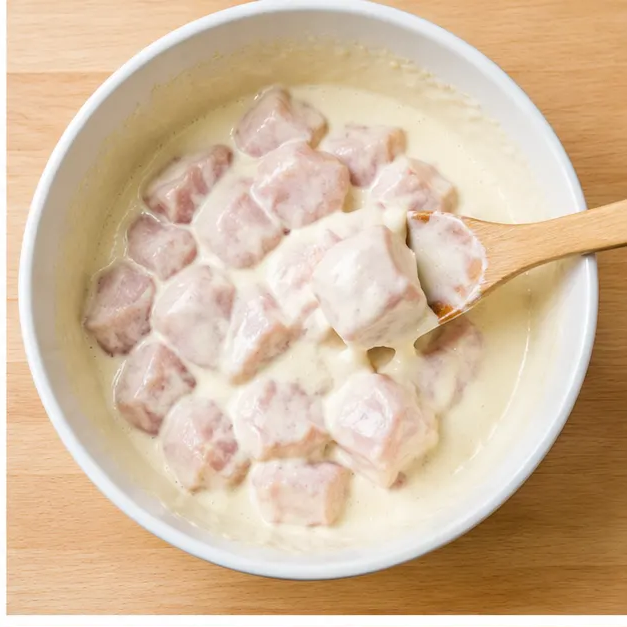 Step 2: Stirring raw cubed plain chicken pieces into a pale seltzer batter until fully coated