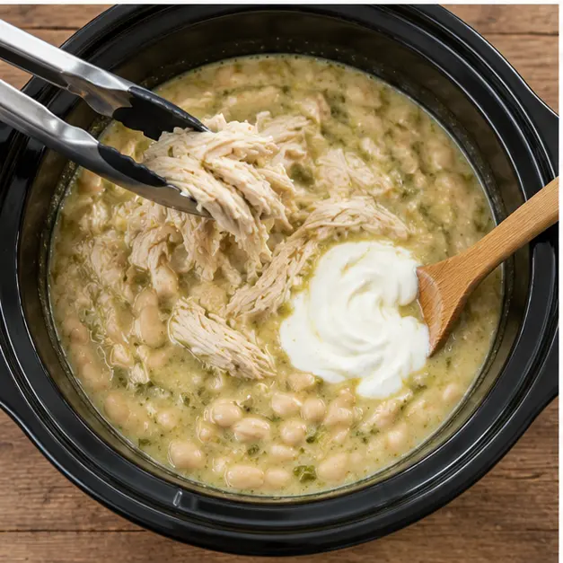 Step 3: Cooked shredded chicken lifted out while white beans and sour cream are stirred into the creamy pot